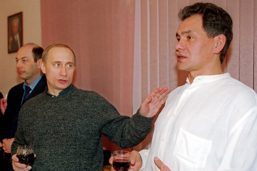 A young Vladimir Putin holds a glass of red while resting his hand on Sergei Shoigu's shoulder