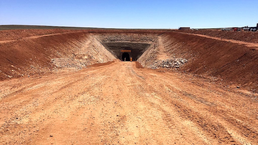 A dirt road leads to a hole in the side of a hill.