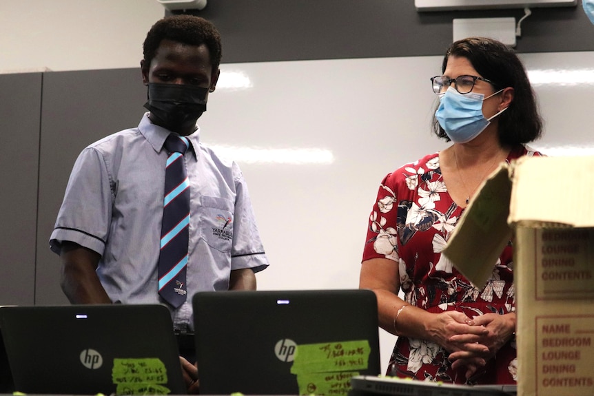A student and a teacher in face masks examining two school computers