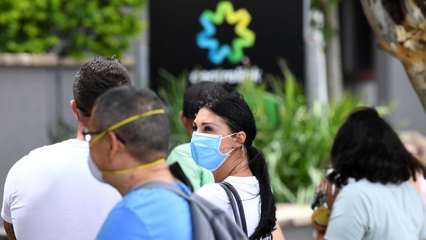 People are seen wearing face masks in a long queue outside the Centrelink office at Southport on Queensland's Gold Coast.