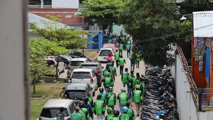 Men in green online taxi jackets walk through a carpark.