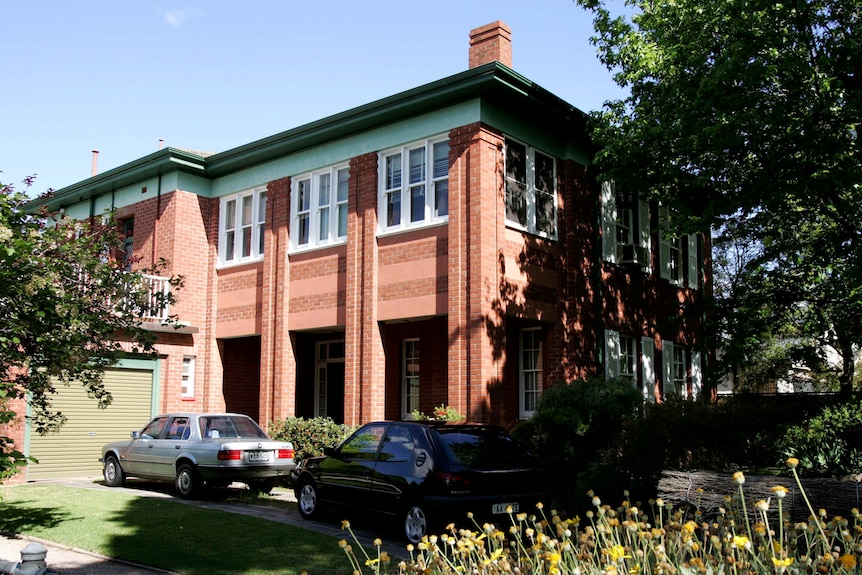 A view of a two-storey red brick building with two cars parked in the driveway. 