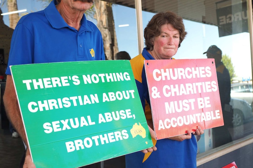 Man and woman stand holding signs that say 'There's nothing Christian about sexual abuse' and 'Churches and must be accountable'