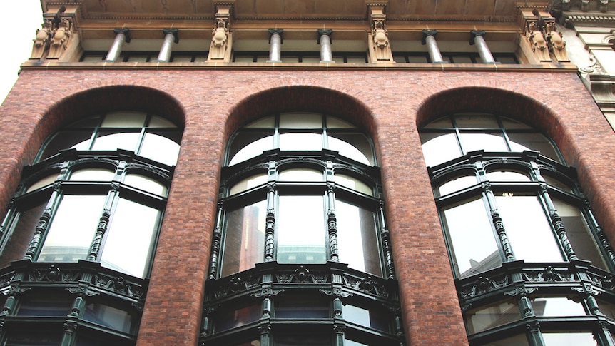 A tall, red-brick building with three large bay windows that each run vertically down three floors.