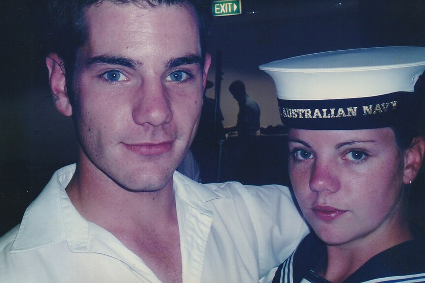 Man with his arm around a woman wearing a naval hat.