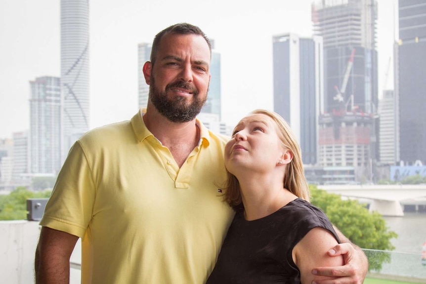 A couple standing together in front of the Brisbane skyline.