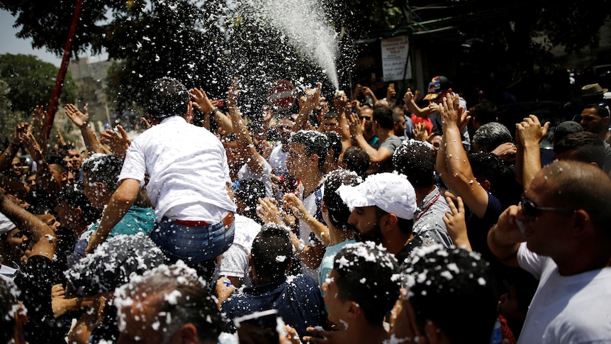 Palestinians celebrate after prayers following the announcement. Some sort of foam is being sprayed as people cheer.