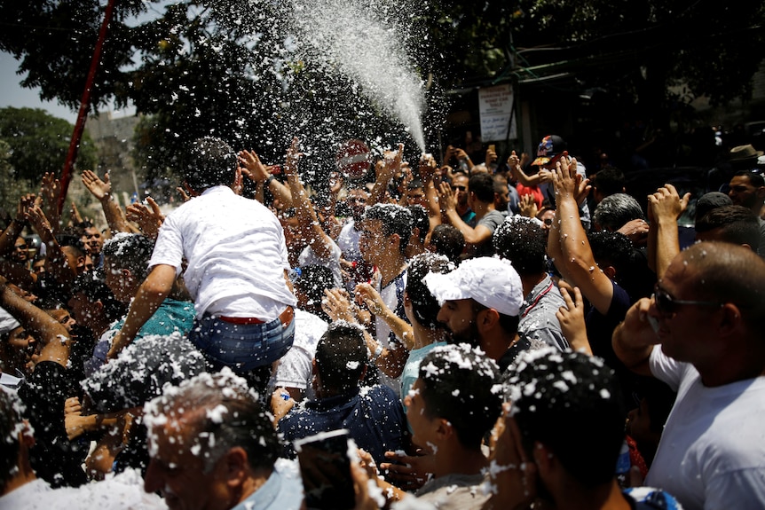 Palestinians celebrate after prayers following the announcement. Some sort of foam is being sprayed as people cheer.