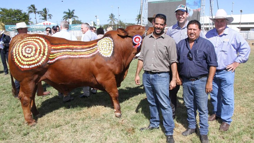 Four men stand in front of a bull that has been painted in an Indigenous style.
