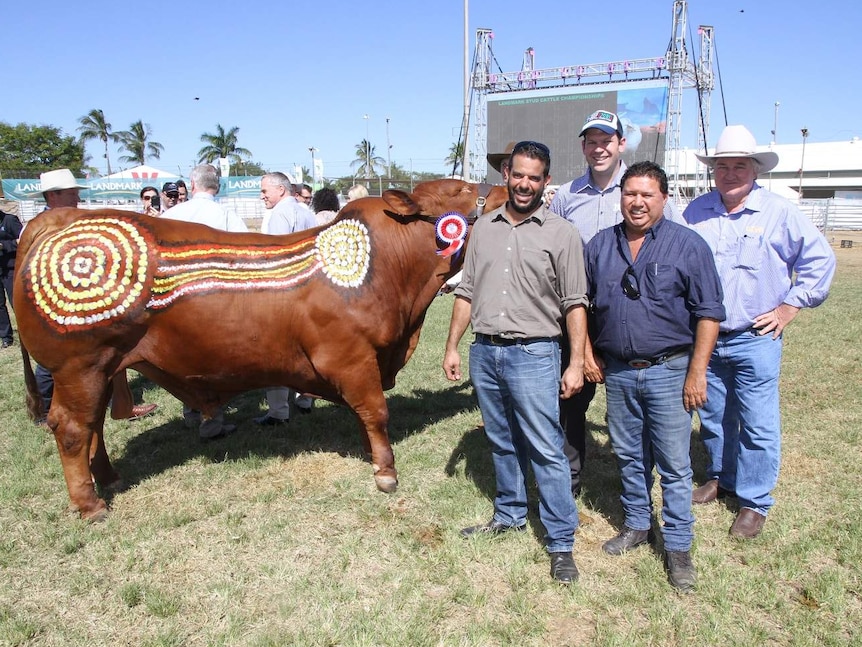 Four men stand in front of a bull that has been painted in an Indigenous style.
