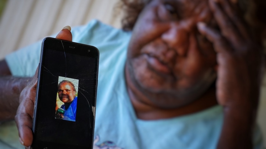 Louise Rankine holds up a phone with a photo of her daughter Sasha Green. Ms Rankhine's other hand is up to her furrowed brow