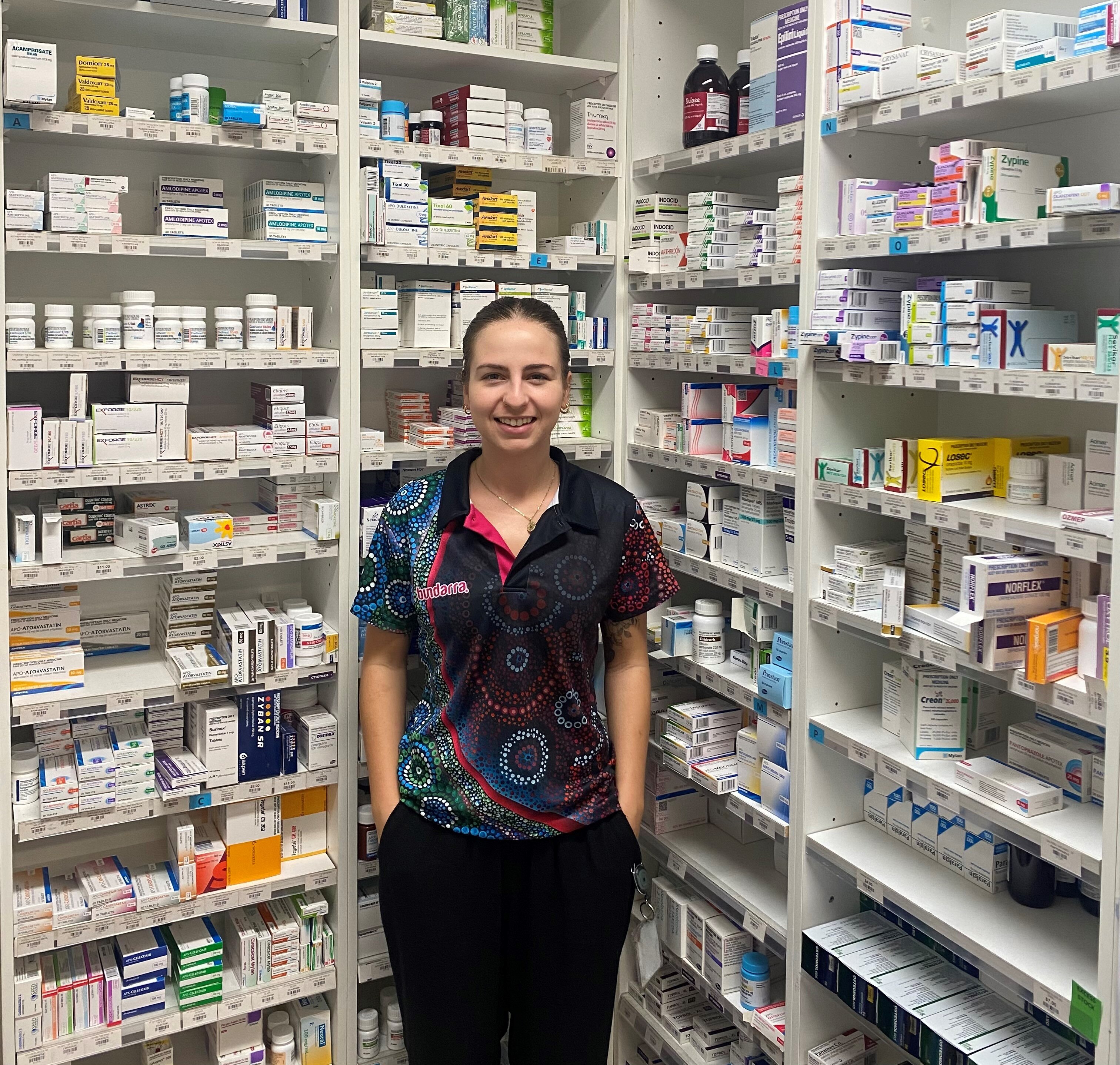 A woman standing in front of a pharmacy shelf full of medication.