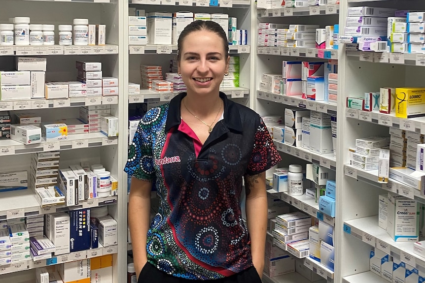 A woman standing in front of a pharmacy shelf full of medication.
