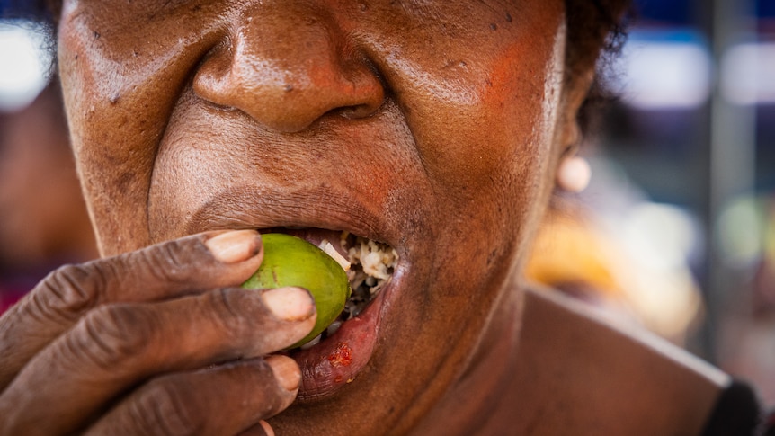 A close-up shows a woman placing a green nut into her mouth