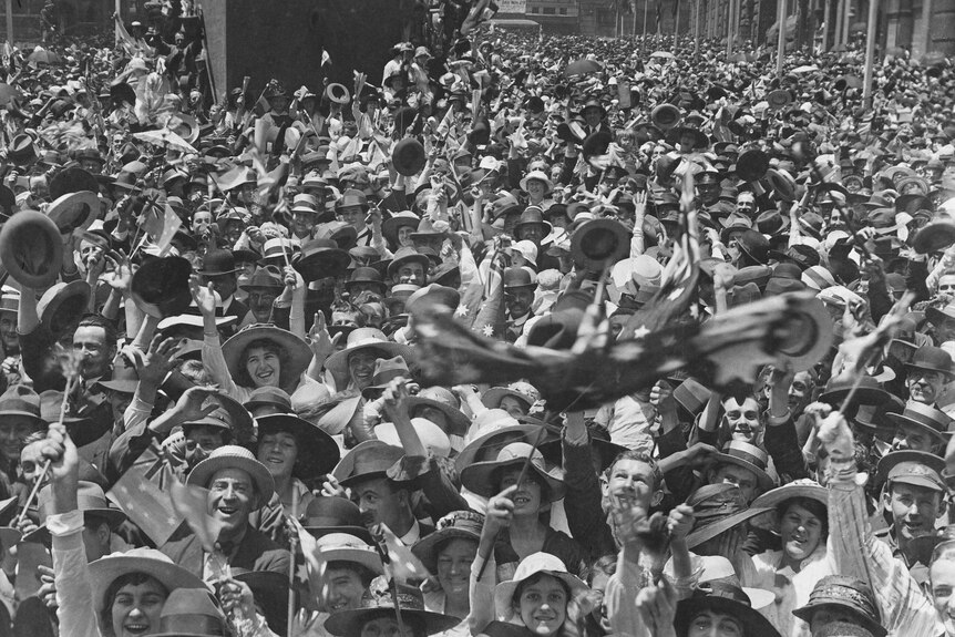 A crowd of hundreds of people gathered in Martin Place, Sydney. They are smiling and waving hats and flags.