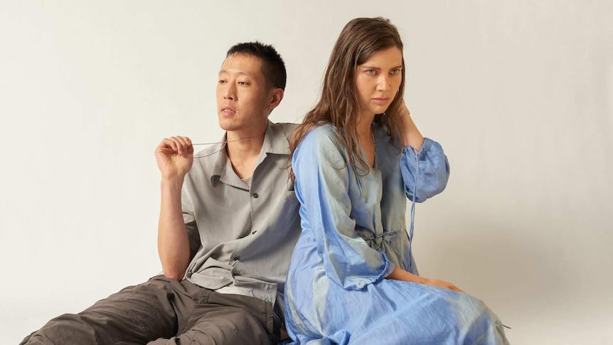 Nigel Yang and Jonnine Standish sitting on the ground in front of a white backdrop.