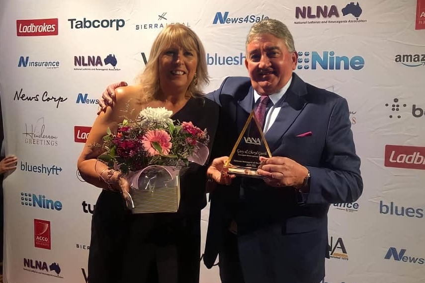 a man in and suit and a woman in a black dress hold a glass plaque and flowers.