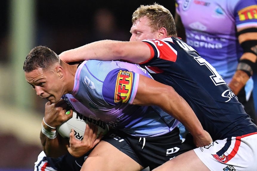 A Cronulla Sharks NRL player holds the ball as he is tackled by Roosters opponents in 2020.