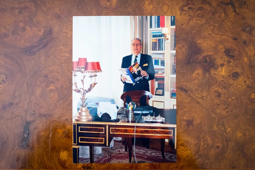 A photograph of an older man in a suit holding a magazine