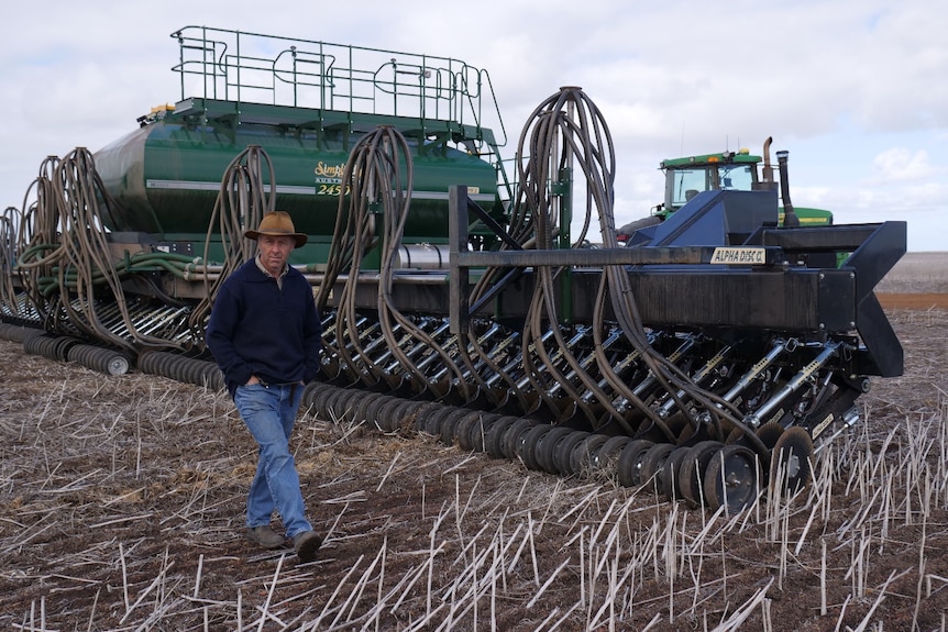 Man walking in front of large agriculture machinery in stubble paddock