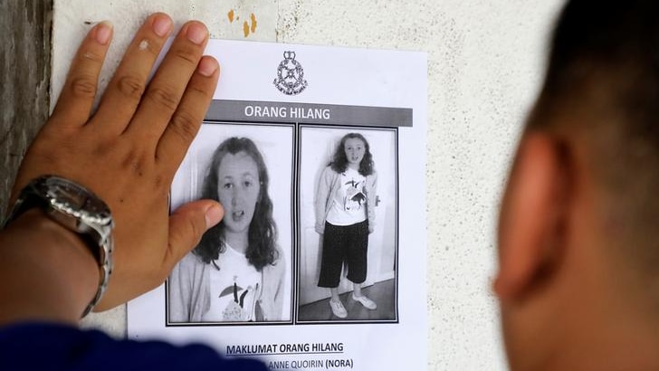 A hand is seen sticking a missing persons poster with two pictures of Nora Anne Quoirin on it, one enlarged.