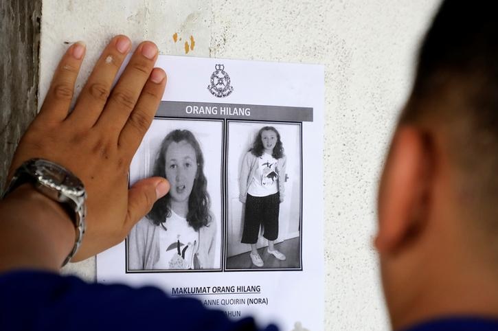 A hand is seen sticking a missing persons poster with two pictures of Nora Anne Quoirin on it, one enlarged.