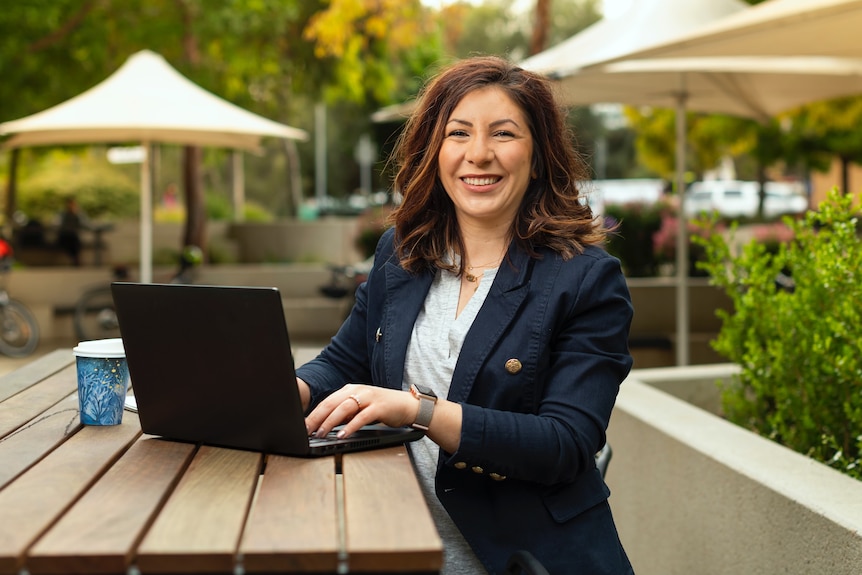 A woman sits with hands on the keyboard of a laptop smiling