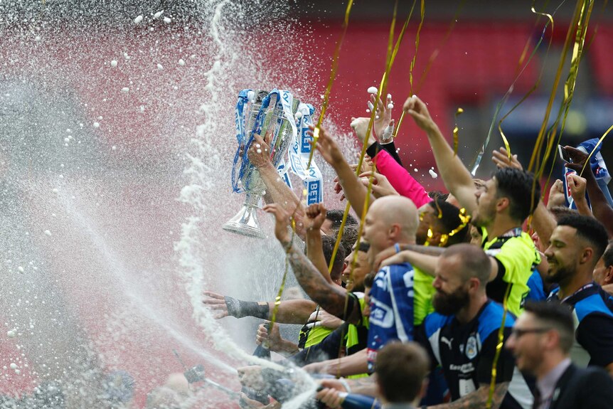 Huddersfield Town players spray champagne and celebrate with the trophy.