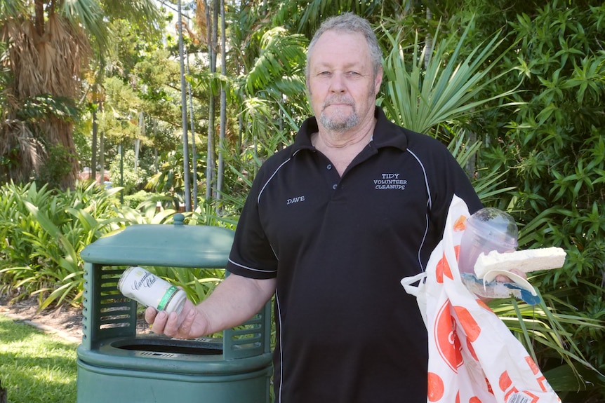Man stands in front of rubbish bin with litter in hand. 