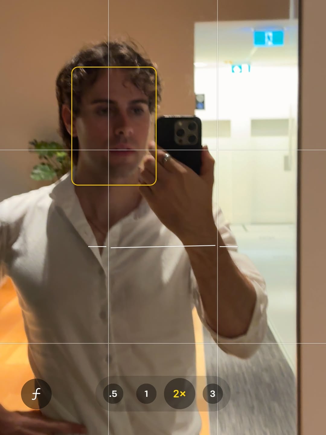 Mirror selfie of a man with dirty blonde hair in a white button up shirt with iPhone camera grid detail
