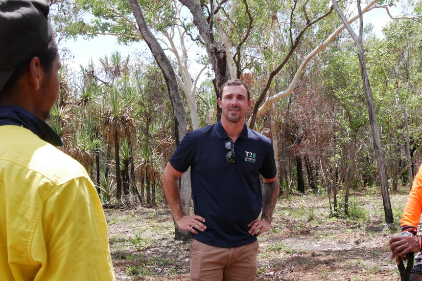 A man wearing a uniform polo shirt speaks with two teenagers wearing fluorescent work shirts.