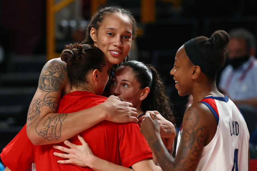 WNBA Basketballer Brittney Griner smiles at the camera while embracing three teammates 