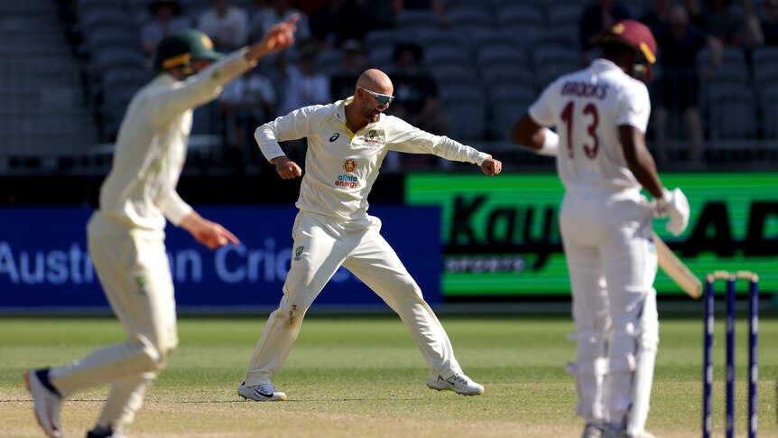 Nathan Lyon punches the air as Marnus Labuschagne appeals in the foreground and Shamarh Brooks stands