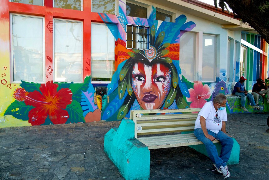 A man sits on a bench in front of a mural.