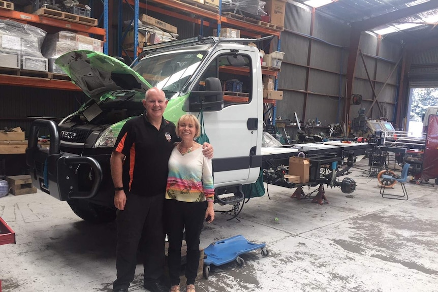 Scott and Anita Bowman smile and pose in front of a truck being fitted out inside a large warehouse.