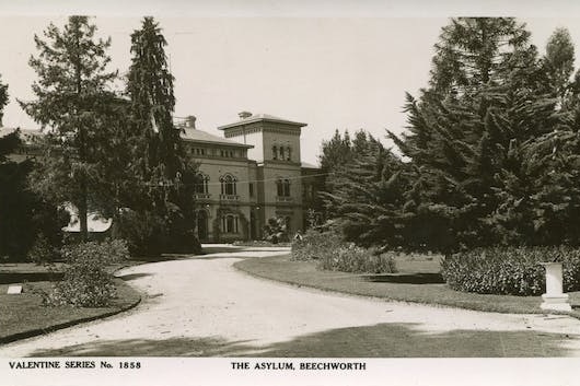 A black and white image of the exterior of a building, surrounded by gardens and trees.