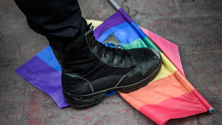 A Turkish riot police officer steps on a rainbow flag.