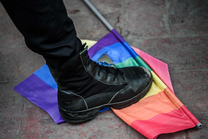 A Turkish riot police officer steps on a rainbow flag.