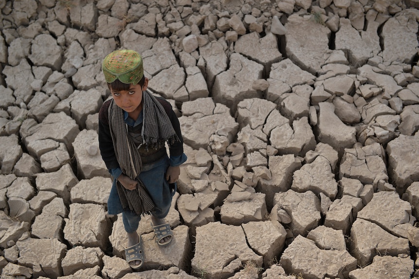A child stands on dry cracked ground.