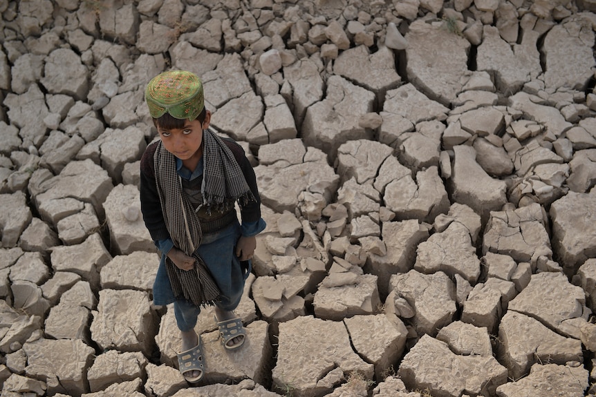 A child stands on dry cracked land.