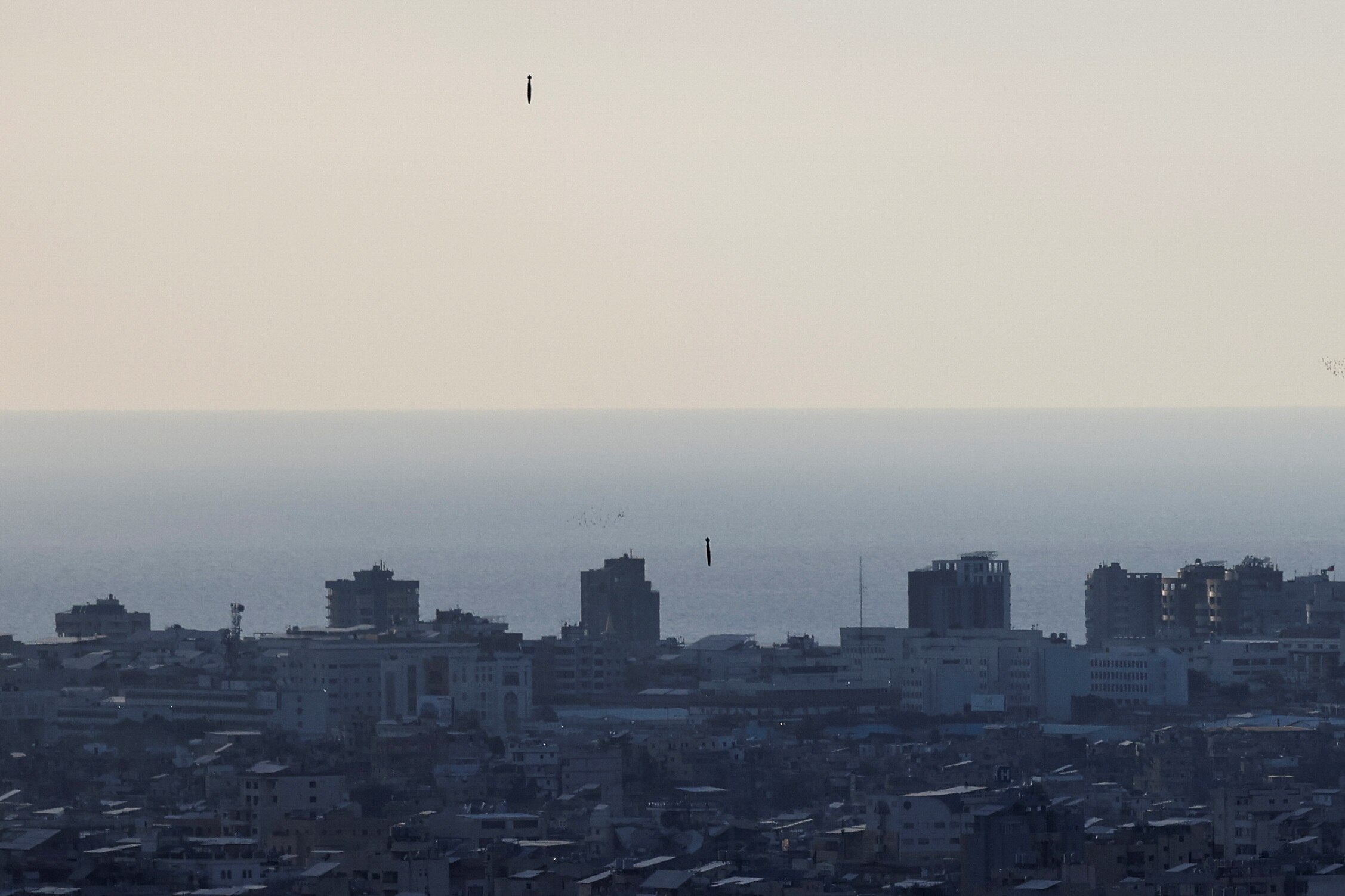 Two missiles falling towards a densely-built-up area of Beirut, with the ocean in the background.
