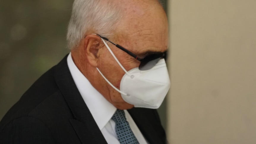 A man wearing a suit, face mask and sunglasses. 
