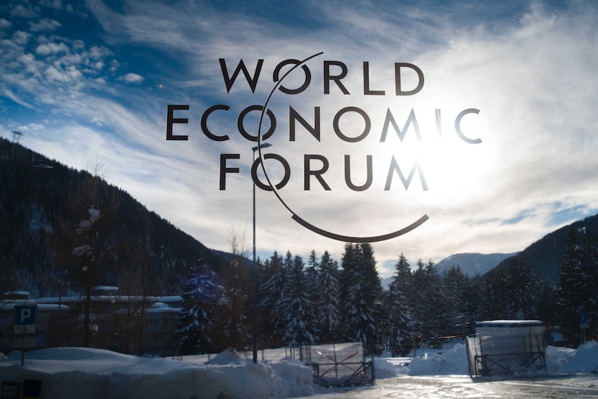 The sign of the World Economic Forum at an entrance at davos in Switzerland with snow in the background.