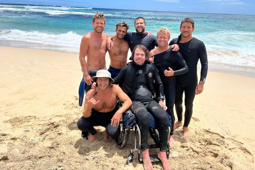 Barney Miller sitting in a wheelchair on a beach surrounded by his friends 