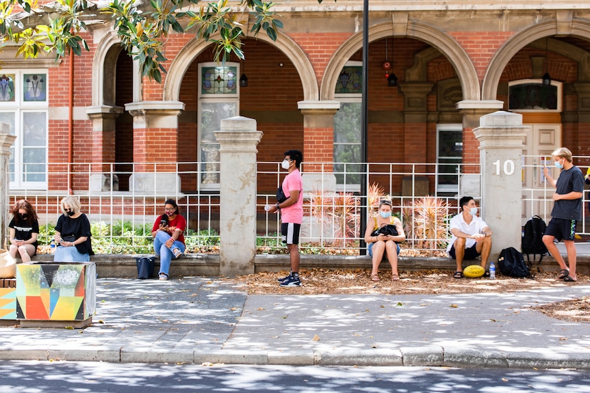 A line of people waiting in front of an old building for a COVID test.