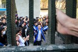 A crowd of protesters in Iran yell and hold their hands in the air.