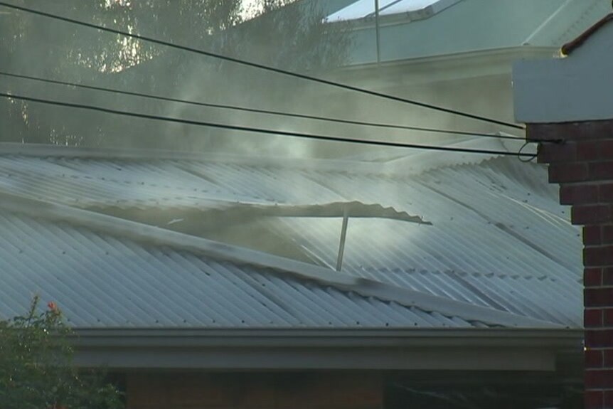Smoke coming from a roof with an old chimney and power lines in the foreground
