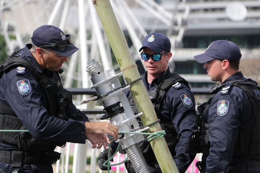 Three officers secure bamboo tripod leg with metal structure.
