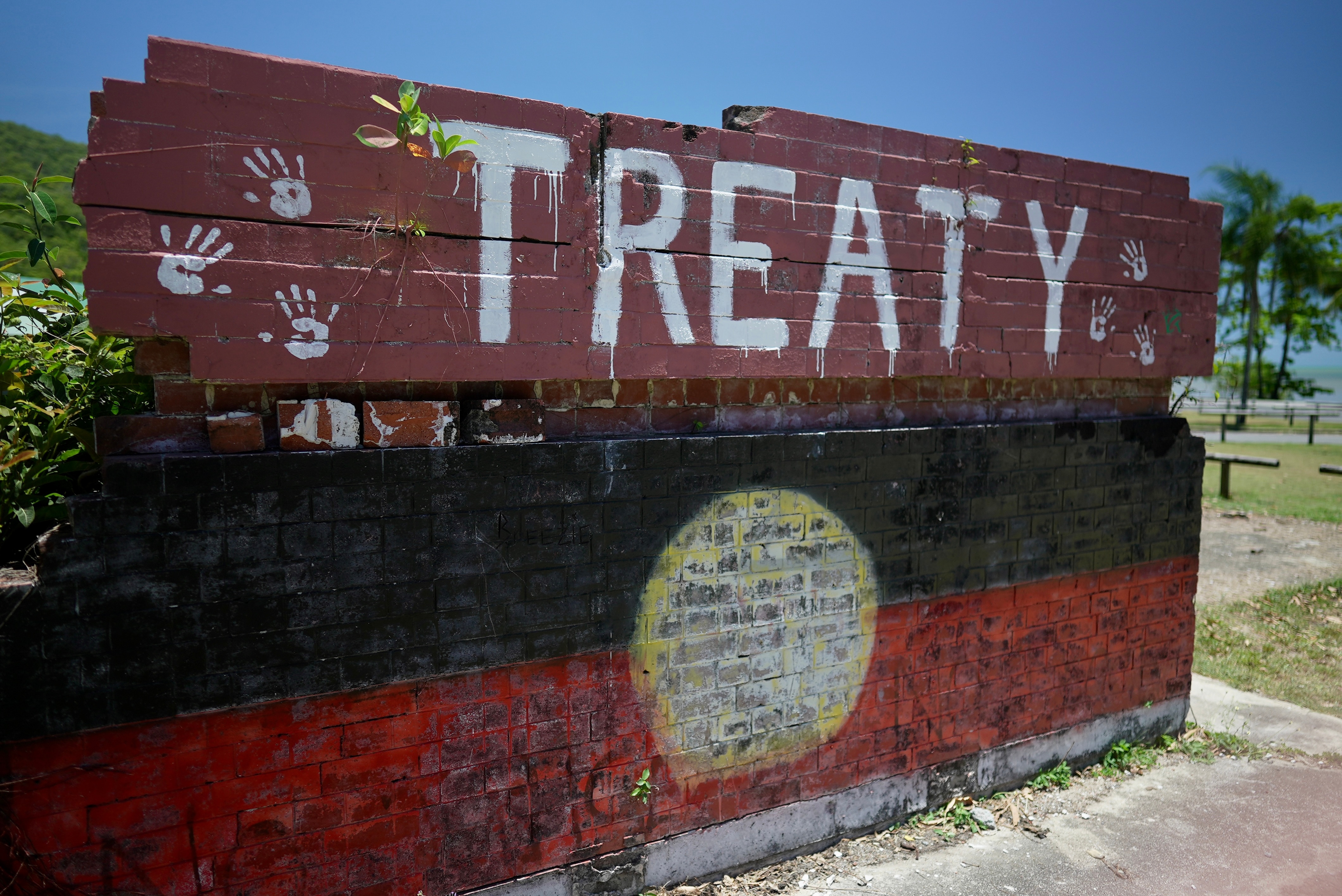 A brick wall says Treaty and has handprints above a painted Aboriginal flag. 