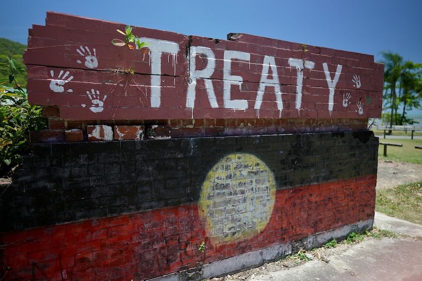 A brick wall says Treaty and has handprints above a painted Aboriginal flag. 